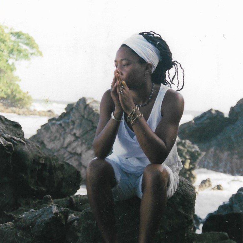 Keshia Abraham sitting on rocks by the sea in Jamaica