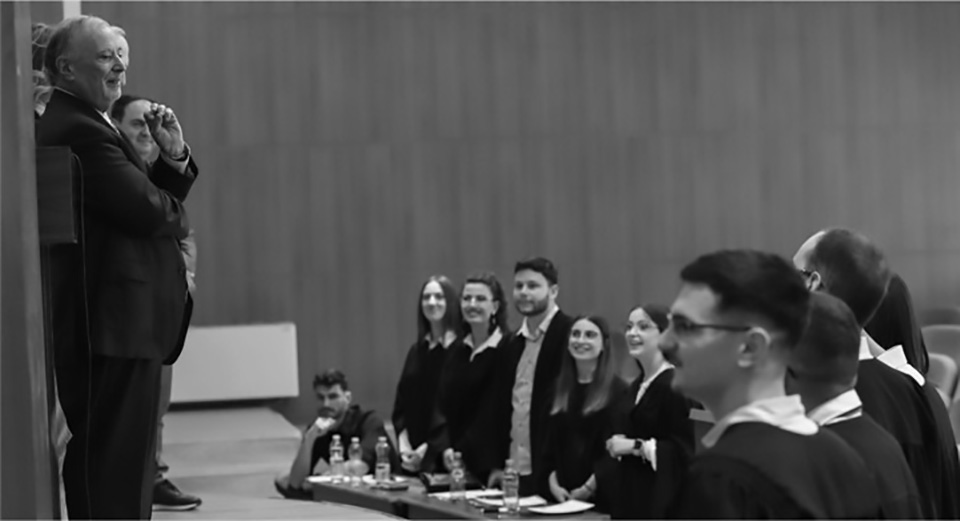 Man standing on stage speaking to students who are standing in audience. 