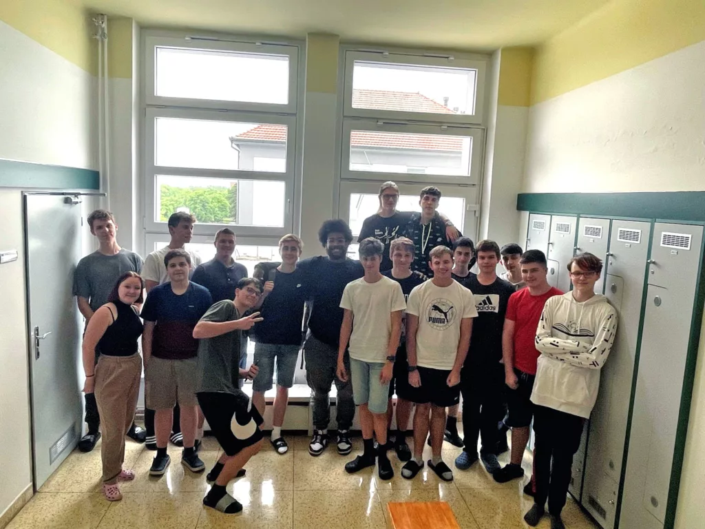Group of male students with teacher standing in locker room in front of a window.