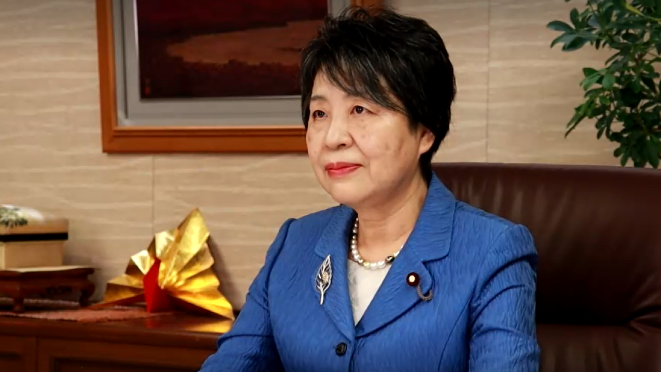 Yoko Kamikawa sitting at desk giving remarks. 