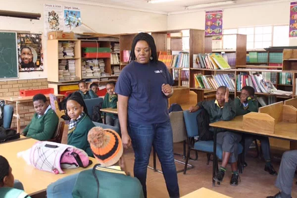 Woman standing in middle of classroom teaching children who are sat at desks,