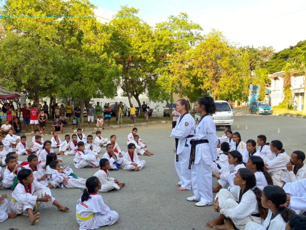 Fulbrighter standing in front of students sitting on floor in karate uniform