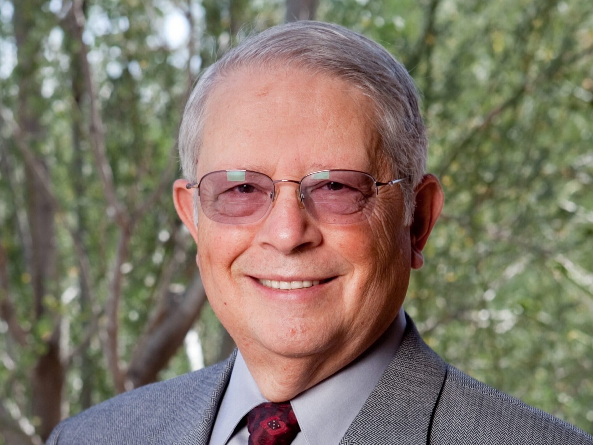 Headshot of a man with glasses, suit, and tie