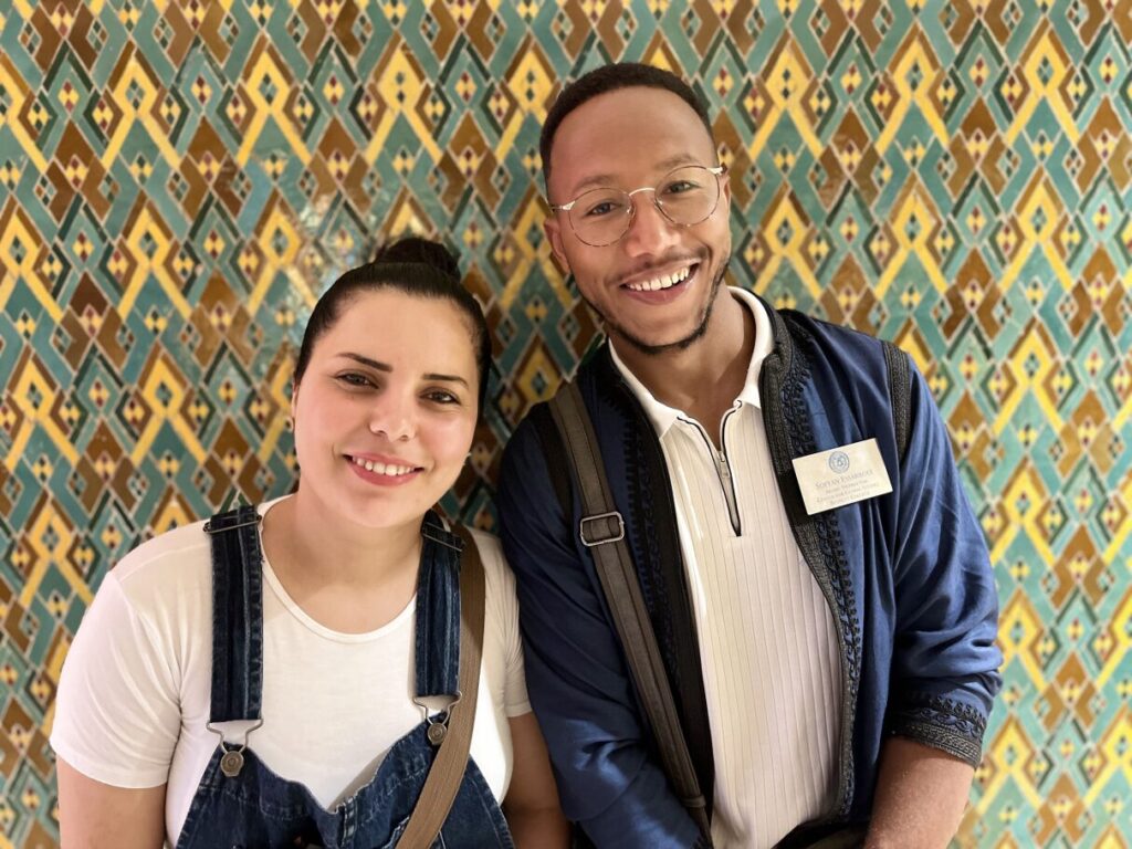 Two people standing in front of wall with patterned wallpaper