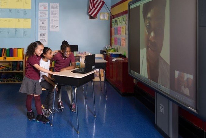 Three young students in classroom watching Fulbrighter on projector.