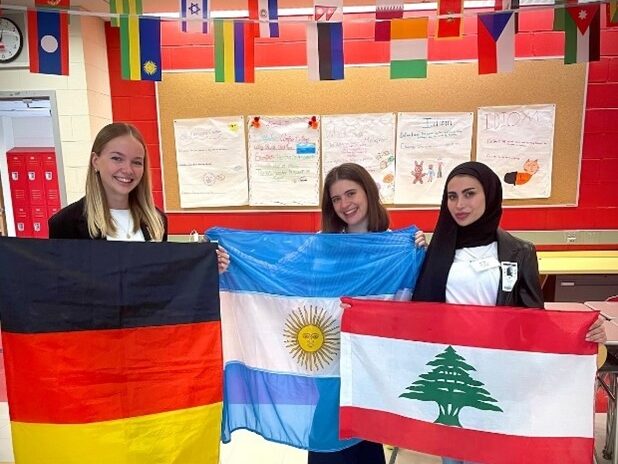 Three students in classroom holding country flags