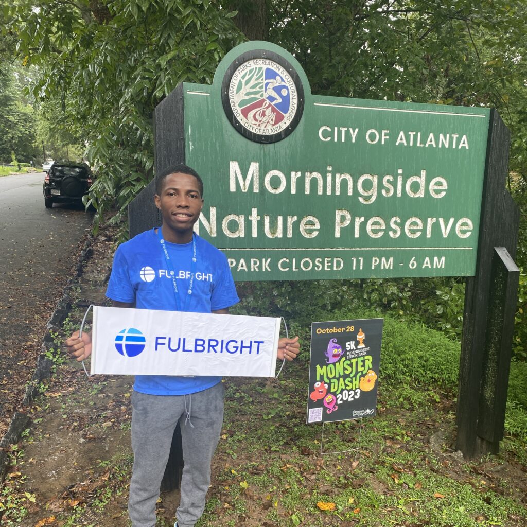 Samuel standing in front of Morningside Nature Preserve sign with Fulbright banner