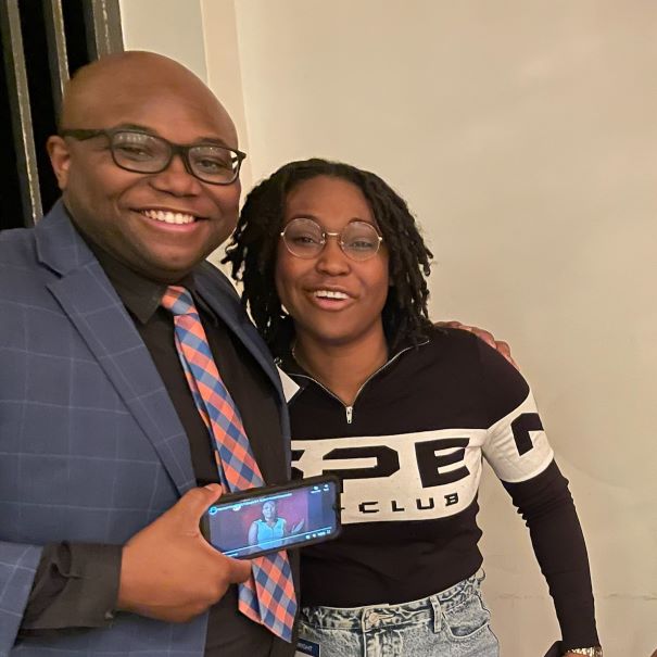 Virgil Parker and Wen-Kuni Céant posing for photo while holding phone with video playing