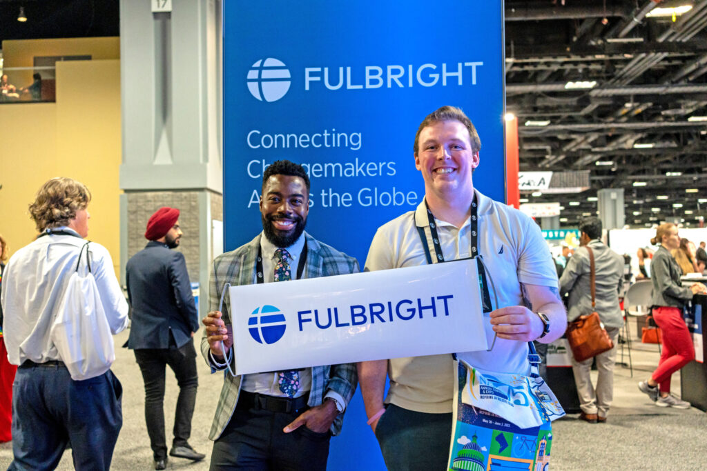 Fulbright Alum and IIE Staff at NAFSA booth standing with Fulbright sign