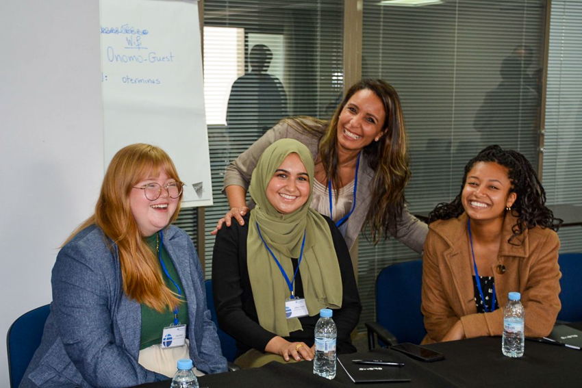 Four people at a table smile for a photo, with a whiteboard in the background.
