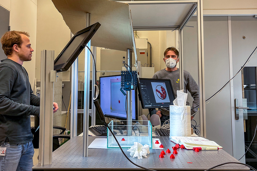 Wilt and a colleague in a laboratory with electronic devices and red cones on a table.
