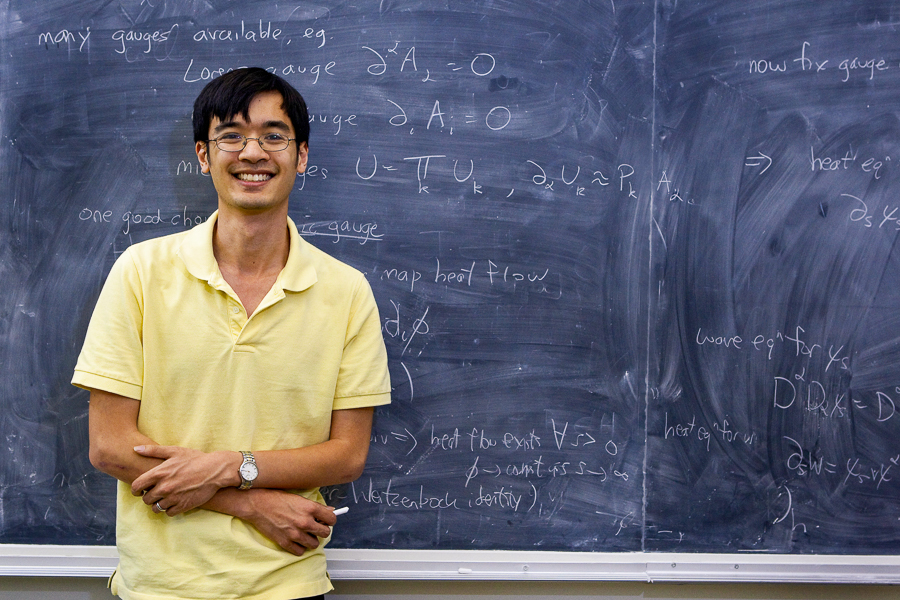 Terrence Tao wearing a yellow polo shirt in front of a black chalkboard.