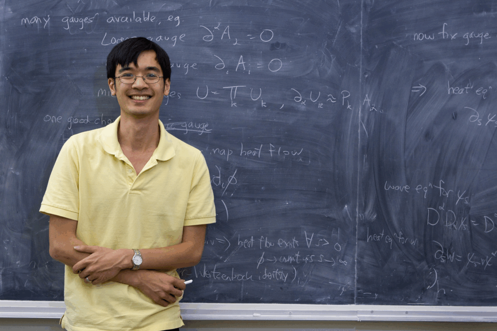 Terrence Tao wearing a yellow polo shirt in front of a black chalkboard.