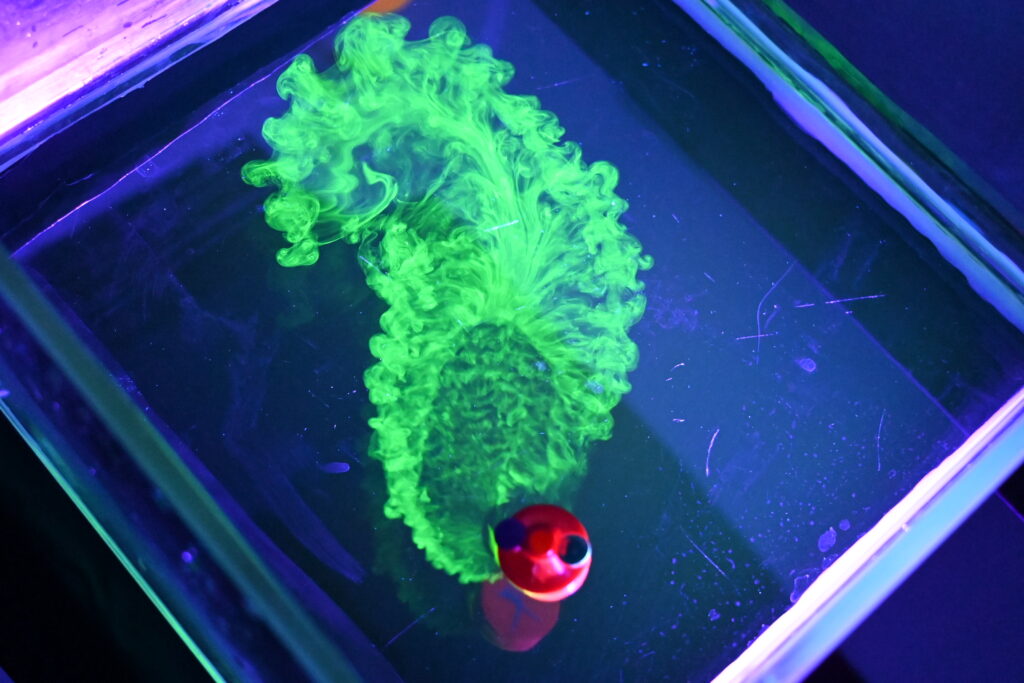 Circular red robot emitting florescent green fumes visible under a UV light.