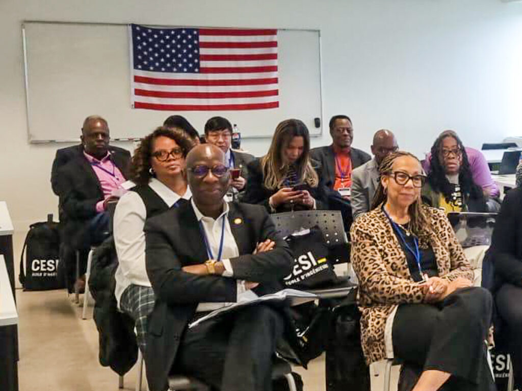 Oscar Barton with group of people seated in a classroom, with an American flag hanging on the wall behind them.