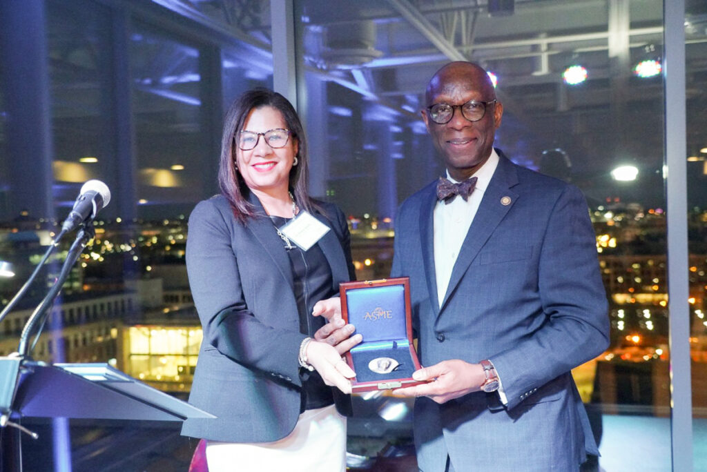 Oscar Barton with woman holding an open award case with a blue interior and a silver medal, standing in front of a nighttime cityscape.