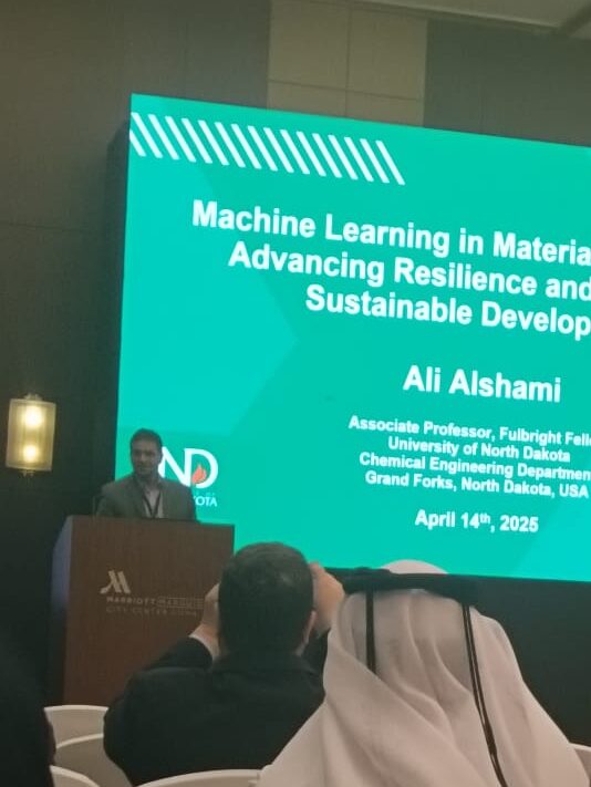 Alshami standing at podium giving a talk with his presentation on a large screen behind him 